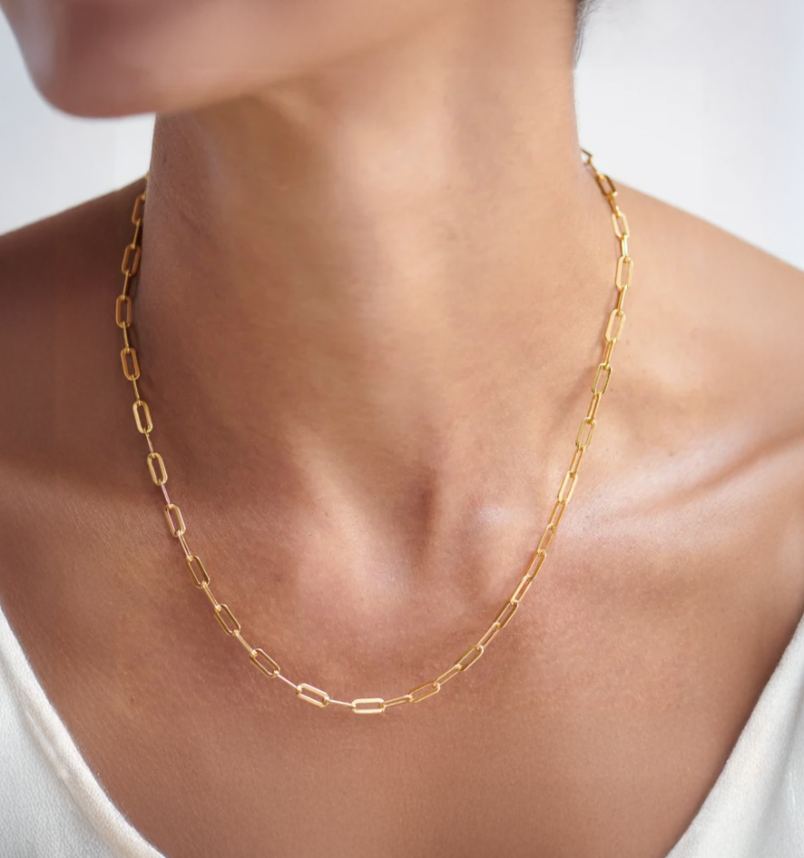 Gold paperclip chain necklace with heart detail worn by a woman